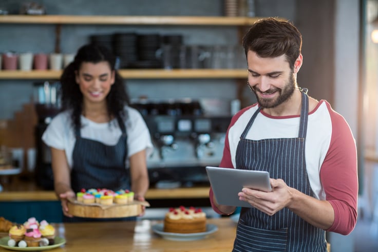 Smiling waiter using digital tablet at counter in cafx92xA9